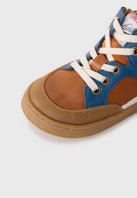 Baskets montantes marron et bleu avec une tige en cuir, des lacets beiges, une semelle en caoutchouc texturée et une marque visible sur le côté.