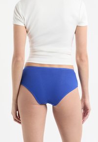 Slip a vita alta blu a costine, con finitura liscia e vita elasticizzata, mostrati di schiena con una maglietta aderente bianca.