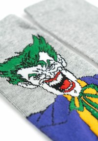 Calze grigie con un design colorato del personaggio Joker. Materiale in tessuto con una superficie liscia. I colori includono verde, bianco, viola e giallo.