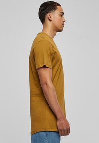 Sennepsgul bomulds-T-shirt med korte ærmer, rund hals og lige pasform, båret med blå denimjeans. Ingen synlige mønstre eller accenter.