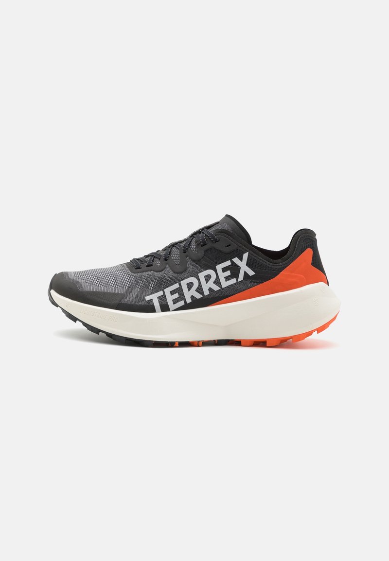 Svarta och grå löparskor med nätövre, vitt "TERREX"-logotyp på sidan, orange detaljer vid hälen och texturerad gummiyttersula.