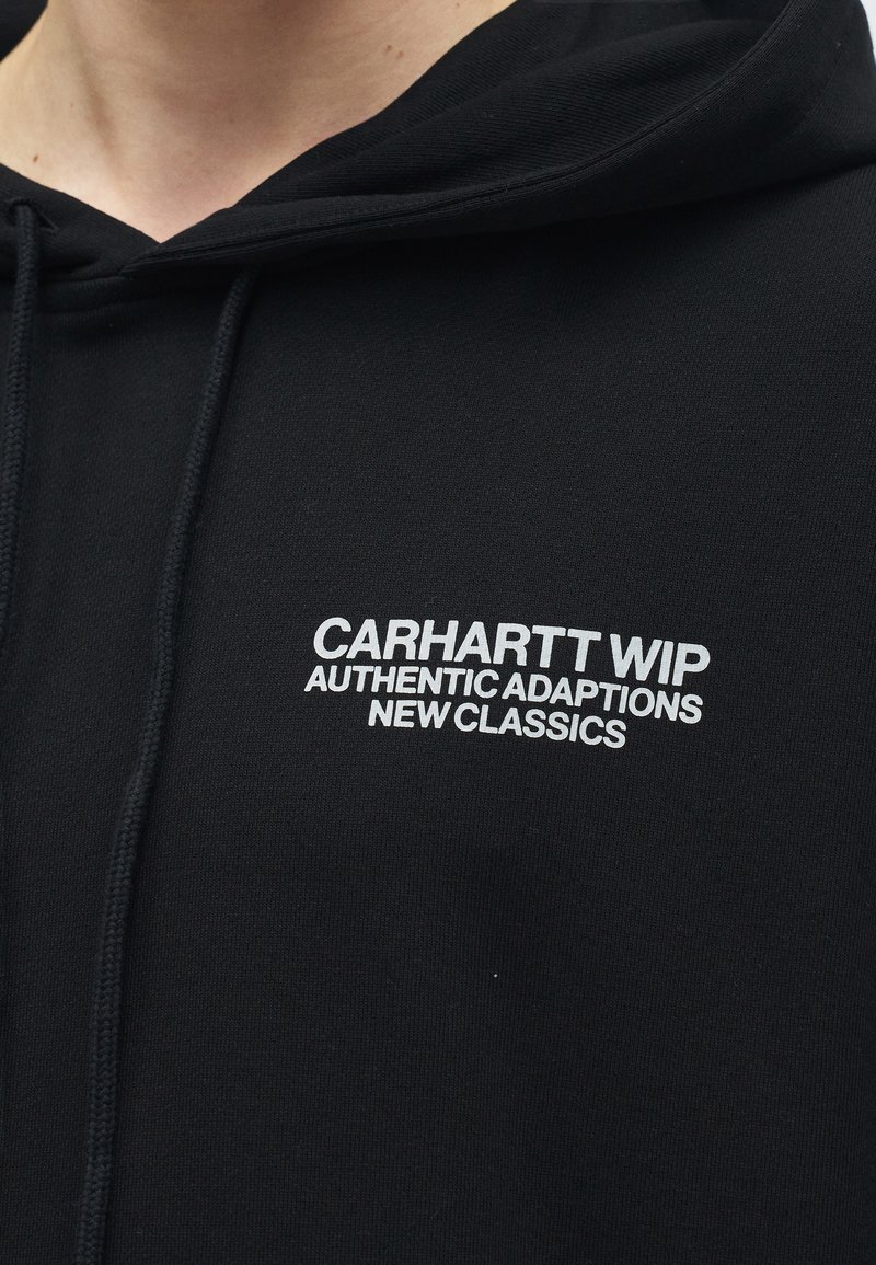 Felpa nera con cappuccio con testo bianco "CARHARTT WIP AUTHENTIC ADAPTIONS NEW CLASSICS" stampato sul petto, vista ravvicinata del busto superiore.