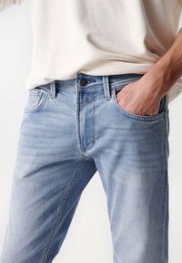 Jeans in denim azzurro chiaro con vestibilità dritta, dotati di tasche frontali, chiusura con bottone nero e delicate pieghe sulla stoffa.