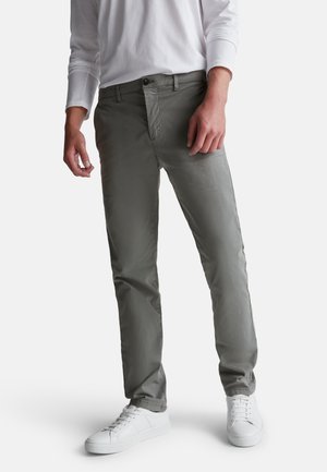 Pantaloni grigi chiari realizzati in tessuto morbido, con vestibilità classica, tasche frontali e chiusura con zip, abbinati a sneakers bianche.