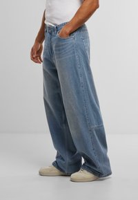 Világoskék, bő szárú farmernadrág, amely enyhe mosási hatással készült denimből, oldalsó zsebekkel és enyhe kopási részletekkel.