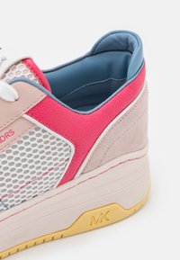 Gros plan sur une chaussure de sport multicolore avec une tige en mesh, cuir rose, daim beige, doublure intérieure bleue, lacets blancs, et une semelle jaune portant la marque "MK".