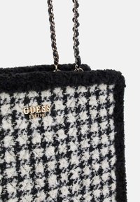 Schwarz-weiße Hahnentrittmuster-Tasche aus strukturiertem Stoff, mit goldfarbenem Logo und Kettenakzent-Trageriemen.
