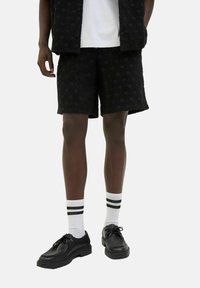 Black textured shorts with a wave pattern, paired with white socks featuring black stripes and black lace-up shoes.