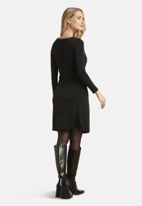 Abito nero a maniche lunghe con silhouette aderente, che arriva a metà coscia. Abbinato a stivali alti in pelle nera lucida fino al ginocchio. Texture liscia.