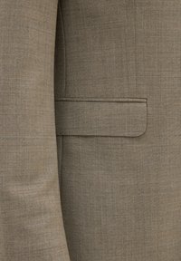Beige blazer van textuurstof, met een subtiel patroon. Voorzien van een gesneden revers en een enkele borstzak aan de linkerkant.