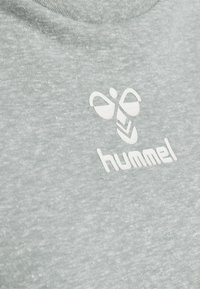 Camiseta gris de brezo con un logo blanco que tiene una abeja y el nombre de la marca "hummel" en una fuente moderna. Tejido suave y texturizado con cuello redondo.