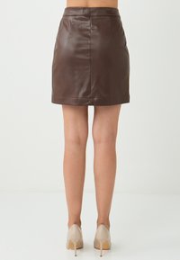 Minigonna in pelle marrone con texture liscia, caratterizzata da una silhouette aderente, cuciture semplici e orlo diritto.