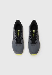Chaussures de sport grises avec un dessus en mesh perforé, des accents noirs et des lacets noirs. Présentent une semelle extérieure jaune vif pour plus de détails.