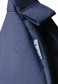 Borsa impermeabile blu navy con tessuto testurizzato e gocce d'acqua visibili. Presenta un'etichetta piccola con icone e un dettaglio di chiusura a patta.