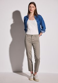 Beige zúžené kalhoty s předními kapsami, doplněné bílým topem a modrou denimovou košilí. Celý outfit doplňují tenisky.