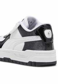 Zbliżenie na czarno-białą piętę sneakersa Puma z teksturowaną podeszwą i przeszywaną białą paską.