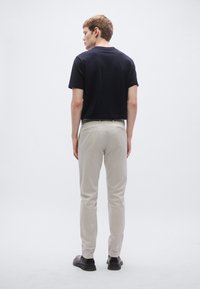 Čierne tričko s krátkym rukávom v kombinácii so svetlo béžovými nohavicami slim-fit strihu a čiernymi topánkami, pohľad zozadu na neutrálnej pozadí.