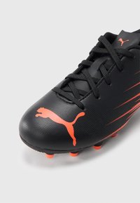 Černý fotbalový kopačky s texturovaným povrchem, červenými akcenty a výrazným logem Puma. Má standardní tkaničky a oranžové kolíky na podrážce.