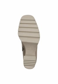 Semelle d'une chaussure beige présentant un dessous en caoutchouc texturé et à motifs, avec des rainures et des crêtes distinctes pour l'adhérence. Marquée du logo de la marque.