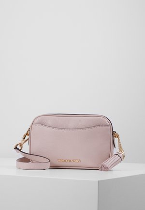 Sac bandoulière en cuir rose clair Michael Kors avec logo doré, sangle amovible et pompon décoratif sur une surface blanche unie.