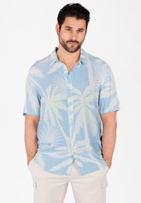 Chemise à manches courtes à boutons en bleu clair avec un motif de feuilles de palmier. Le tissu est lisse, présente un col et une coupe décontractée.