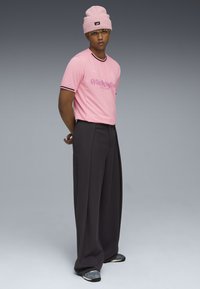 Camisa rosa de manga corta con ribete negro y estampado gráfico, combinada con pantalones anchos negros y zapatillas grises. Texturas suaves y lisas.