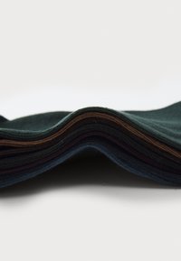 Pile de morceaux de tissu pliés en vert foncé, marron, noir et bleu, montrant des bords texturés et des couleurs variées avec des surfaces lisses.