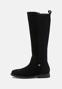 Black knee-high boot with a suede front and ribbed textile sides. Features a low, flat sole and a gold accent near the ankle.