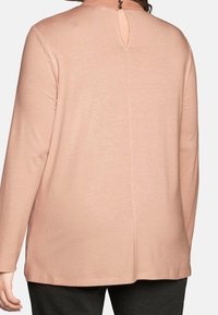 Långärmad topp i mjuk rosa tyg. Har en rund halsringning med ett nyckelhål baktill och rak nederkant. Slät textur.