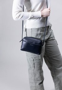 Navy Leder Umhängetasche mit Reißverschluss, glatter Textur und schlankem rechteckigem Design, das ein leichtes Logo-Detail auf der Vorderseite aufweist.
