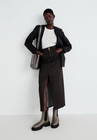 Chaqueta de cuero negra, camisa blanca con estampado de leopardo, falda marrón de talle alto con una abertura, y botines grises con suelas negras. Bolsa gris.