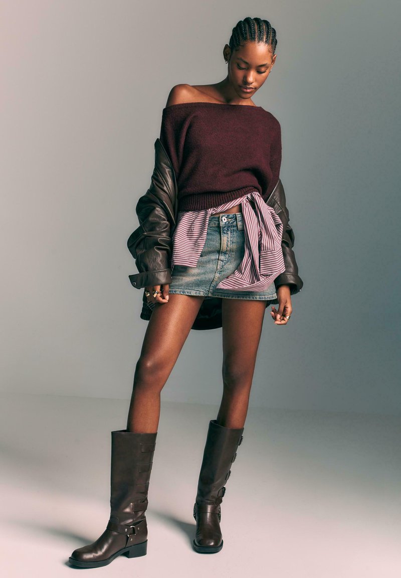 Bordo pulover z odprtimi rameni, slojevita jeans krila s prugastim metuljčkom, rjave usnjene čevlje do kolen z zaponkami.