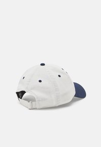 Cappellino da baseball bianco con visiera blu navy, sei fori di ventilazione e strap regolabile sul retro. Tessuto liscio.