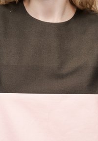 Άνω μέρος κορμού ατόμου που φοράει ενδυμασία δύο τόνων με σκούρο καφέ πάνω μισό και ανοιχτό ροζ κάτω μισό.