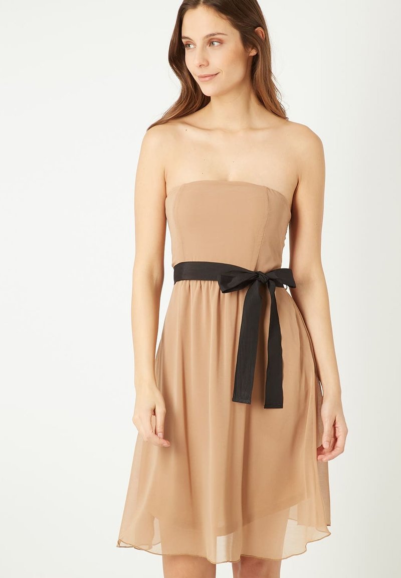 Vestido sin tirantes, de longitud hasta la rodilla, en suave tela beige con un cuerpo ajustado. Cinturón de satén negro atado a la cintura, creando una silueta fluida.