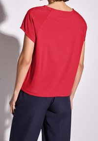 Röd kortärmad topp med rund halsringning, slät textur och avslappnad passform. Matchad med mörkblå vida byxor.