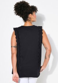 Top senza maniche nero con bordo in pizzo scallop lungo le spalle e i lati, realizzato in un materiale morbido con una vestibilità comoda.