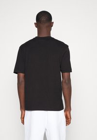 Maglietta nera in cotone con scollo rotondo, maniche corte e taglio dritto, vista da dietro. Tessuto liscio, senza motivi o dettagli.