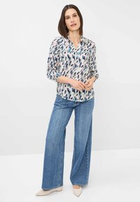 Leichte Bluse mit einem mehrfarbigen abstrakten Muster, Knopfleiste und Dreiviertelärmeln, kombiniert mit weiten blauen Denim-Jeans.