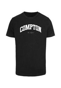Sort bomulds t-shirt med "COMPTON" i fede hvide bogstaver og "Los Angeles" i mindre kursivtekst nedenunder. Korte ærmer, rund halsudskæring.