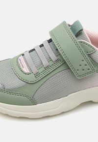 Grüner Sportschuh mit atmungsaktivem Mesh-Obermaterial, elastischen Schnürsenkeln, Klettverschluss und pinkem Innenfutter. Strukturiertg Gummisohle für Grip.