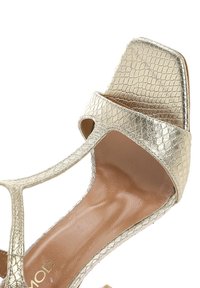Sandale T-strap en or, texturée, avec un bout carré et des côtés ouverts. Semelle intérieure lisse et accents en matériel minimaux.