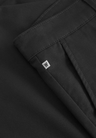 Pantalon noir en tissu lisse et texturé. Doté d'une taille repliée et d'une petite étiquette blanche sur le côté. Design simple, sans motifs.