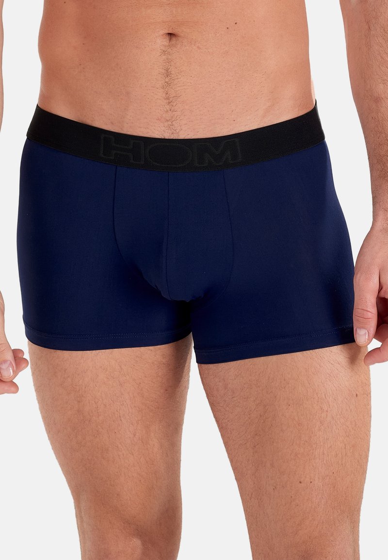 Marineblauwe heren boxershorts van zacht stof met een zwarte elastische tailleband waarop de merknaam "HOM" in reliëf staat.