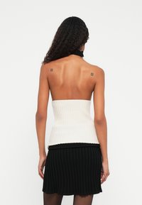 Top de tubo tricotado com nervuras em creme, com um design justo, combinado com uma saia mini plissada preta. Textura suave, sem ferragens visíveis.