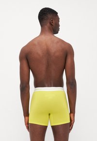 Helle gelbe Boxershorts aus strukturierter Baumwolle mit elastischem, weißem Logo-Bund und taillierter Passform, aus der Rückansicht präsentiert.