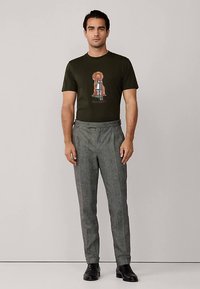 Oliivinvihreä lyhythihainen t-paita, jossa koirakuosi, yhdistetty harmaisiin ruutuhousuihin ja mustiin kenkiin. Yksinkertainen, istuva malli.