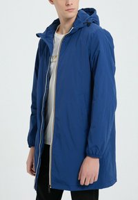Veste à capuche légère bleue avec des poignets élastiques, fermeture éclair sur toute la longueur à l'avant et accents contrastés jaunes et blancs. Elle dispose de poches latérales et a une coupe décontractée.