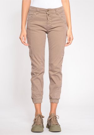 Pantalons cropped beige à jambe fuselée, en tissu mélangé coton, avec deux poches avant et des poignets élastiques. Associés à des baskets vertes.