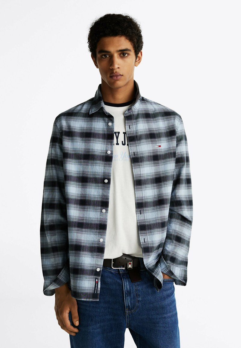Camisa de cuadros de botones en colores negro, blanco y azul. Tejido suave con mangas largas y un corte relajado, llevada sobre una camiseta gráfica.